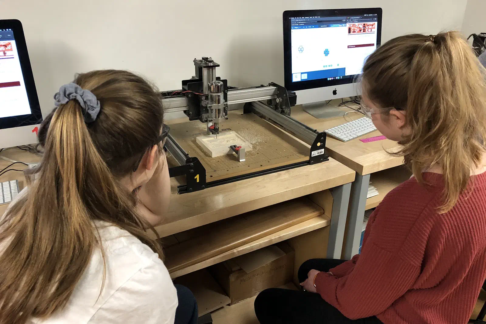 Two students seated at an X-Carve with Easel open on the iMac beside it.