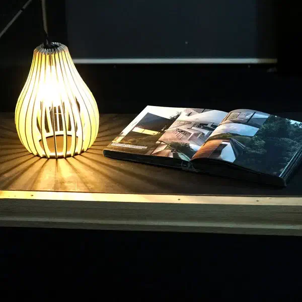 A slatted hanging lamp lighting a magazine on a table in a dark room.