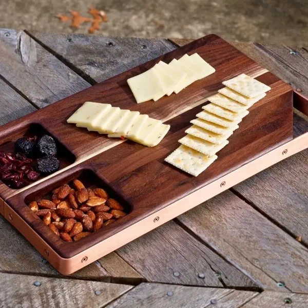A walnut serving board with cheese, crackers, nuts and fruit arranged on it.