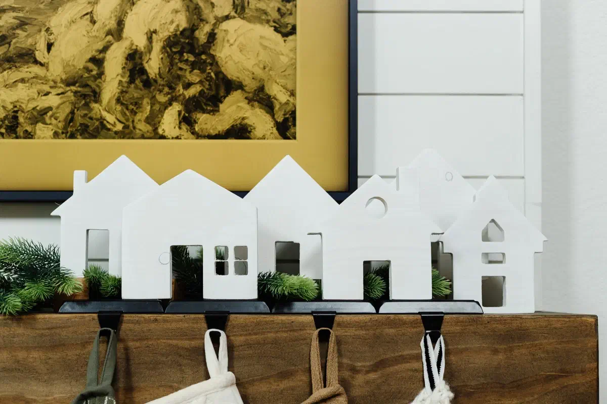 Complete white wooden village silhouettes arranged on a wooden mantel with stockings below