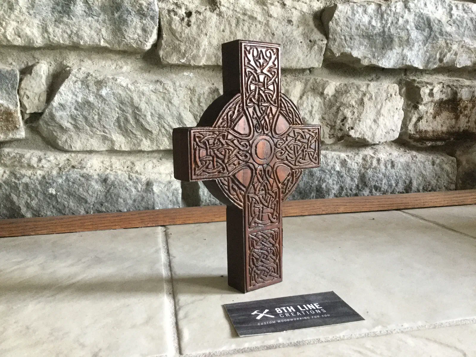 Complete dark walnut Celtic cross standing against a stone wall