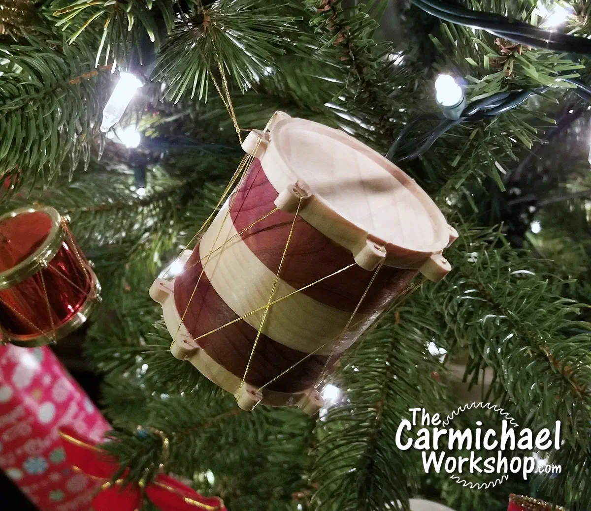 Red-and-pale wooden drum ornament wrapped in gold thread on a Christmas tree