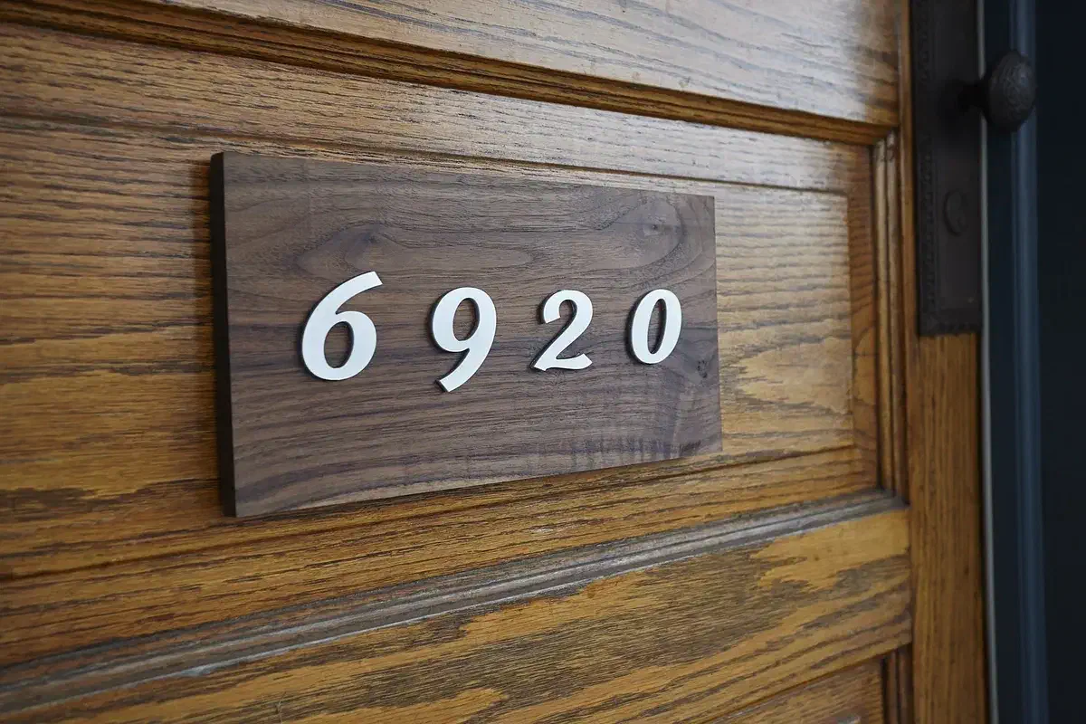 Finished walnut address marker with raised white acrylic 6920 numbers mounted beside a door