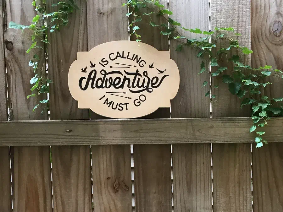 Finished wood Adventure Is Calling sign displayed on a garden fence