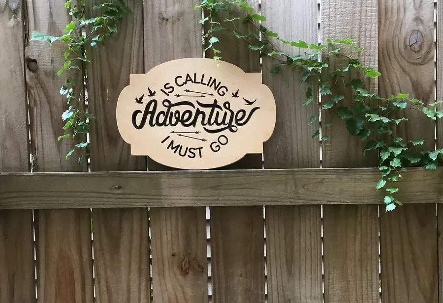 Finished wood Adventure Is Calling sign displayed on a garden fence