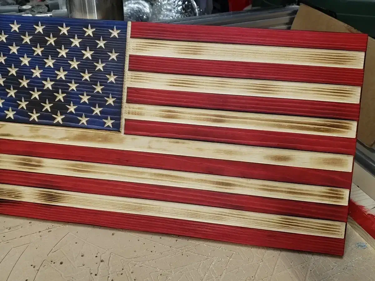 Finished red, white, and blue wooden American flag with carved stars and scorched natural wood stripes
