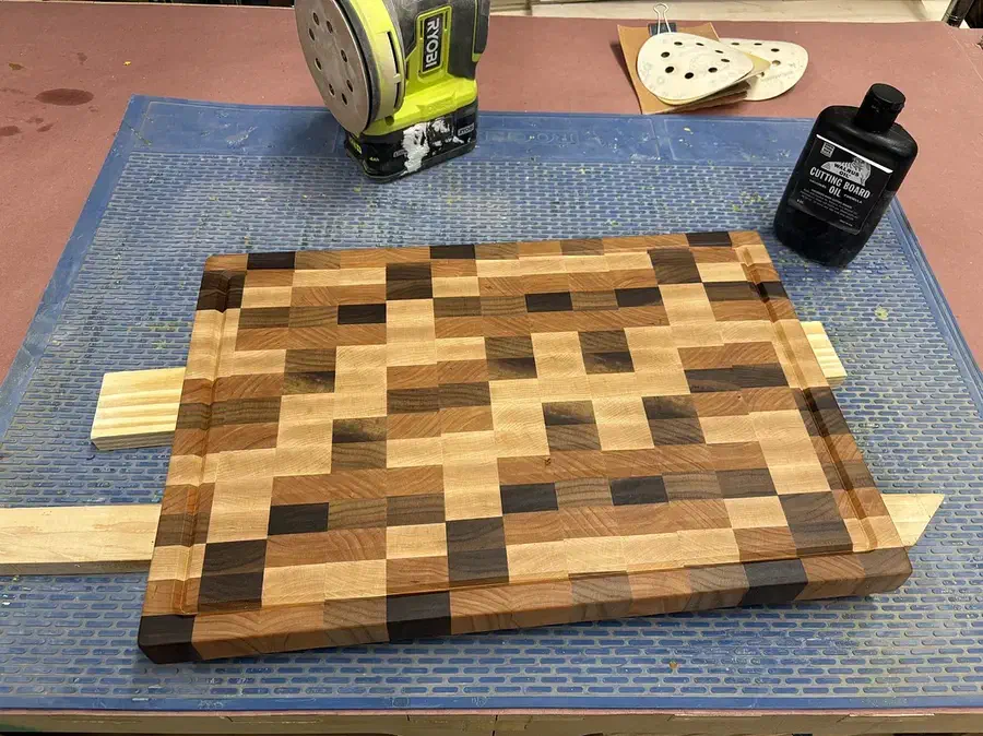 A finished end-grain wooden cutting board with a perimeter juice groove on a workshop bench