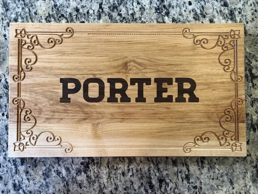 A finished pale maple cutting board with dark walnut PORTER lettering and a carved ornamental border