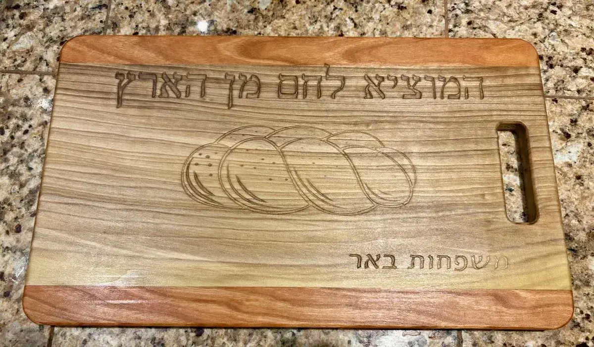 A finished wooden bread board engraved with Hebrew lettering and a braided loaf illustration