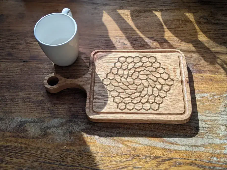 A finished wooden handled board with a swirling hexagon pattern carved across its face