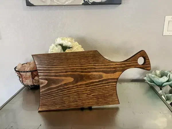 A finished wooden serving board shaped like a wide cleaver with a hole through its handle