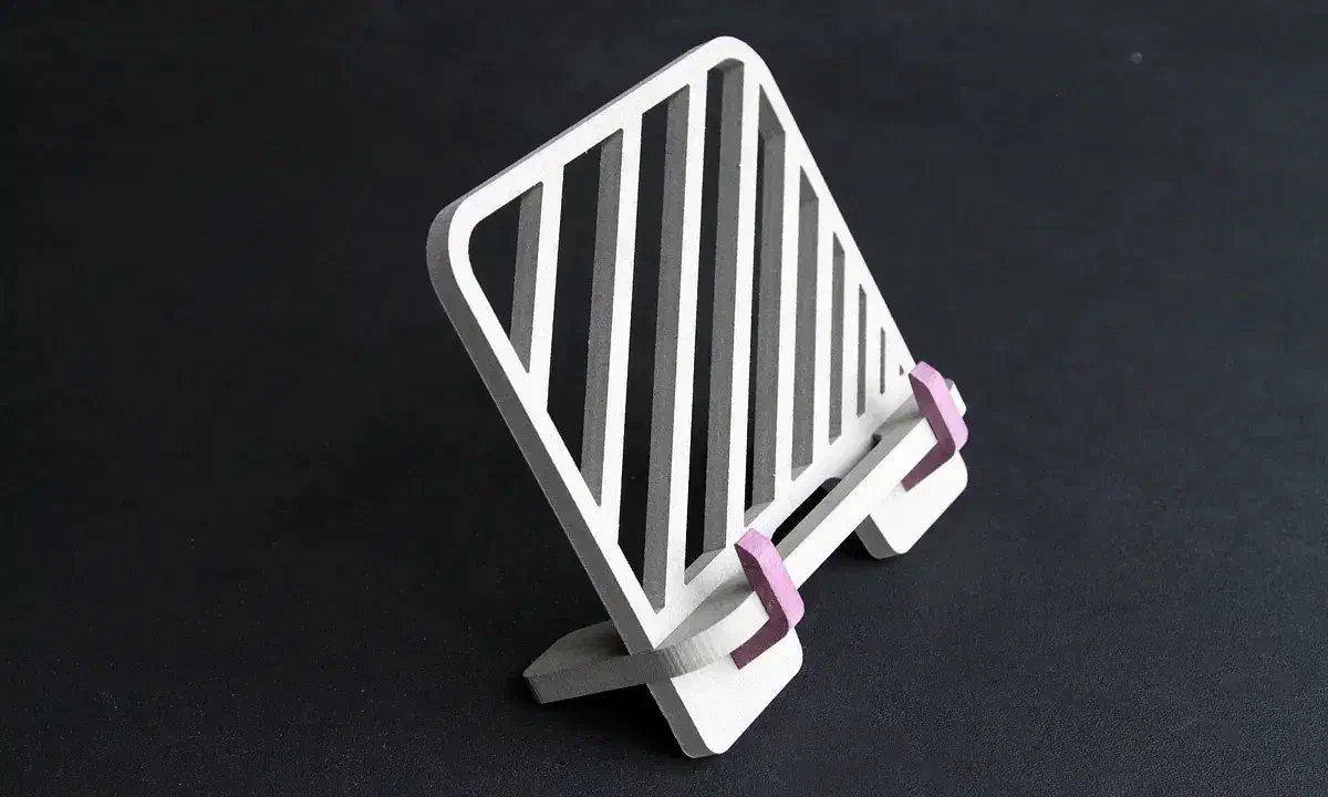 A pale MDF book stand with diagonal carved stripes and purple page hooks