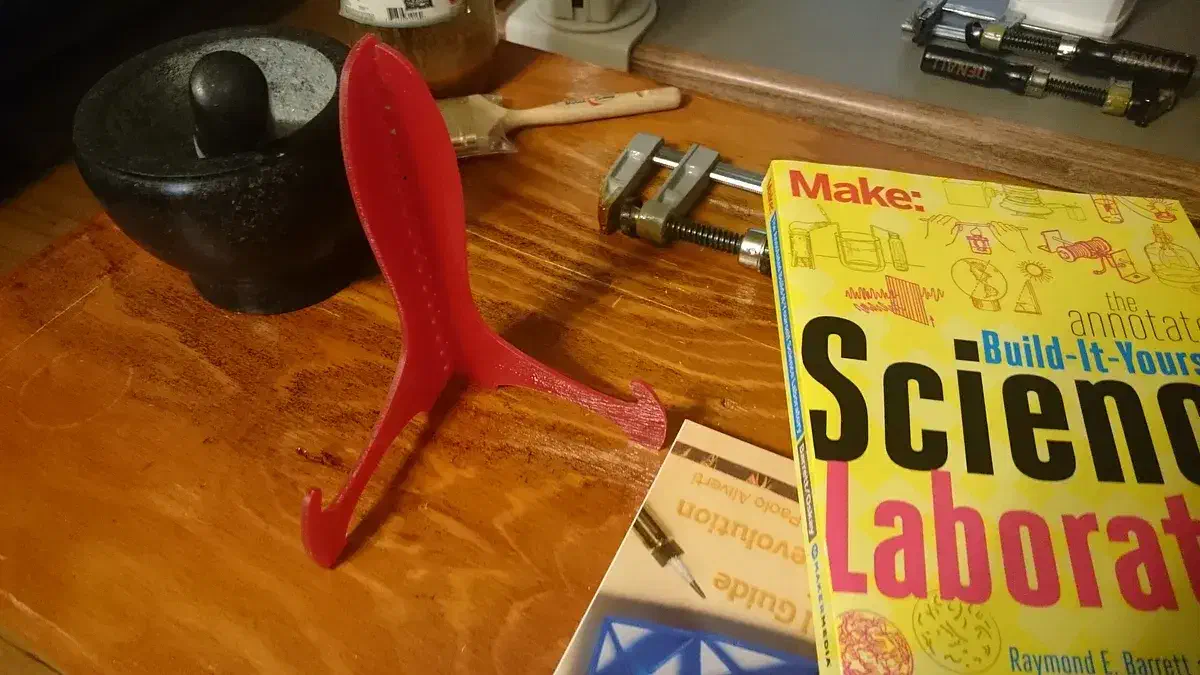 A red two-piece acrylic book stand on a workbench beside books