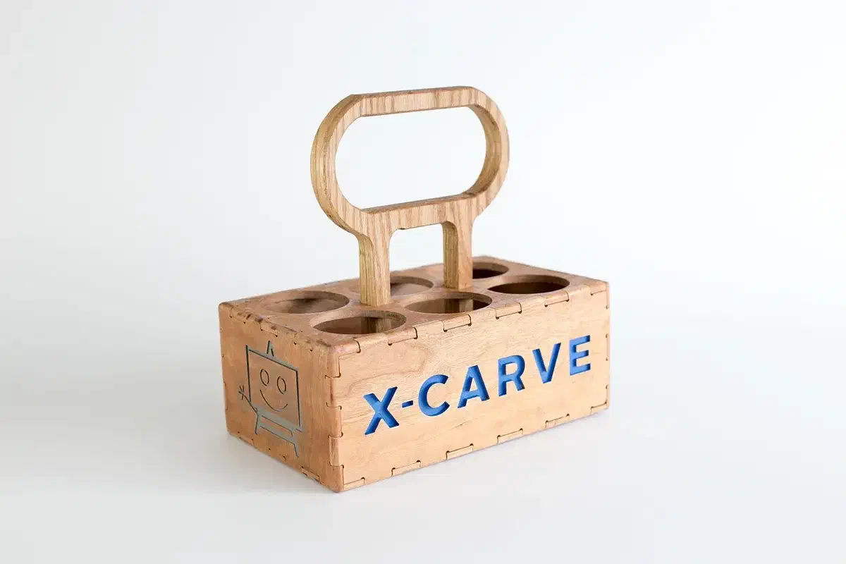 Finished wooden six-bottle carrier with a curved handle, circular bottle openings and blue X-CARVE lettering on a white background