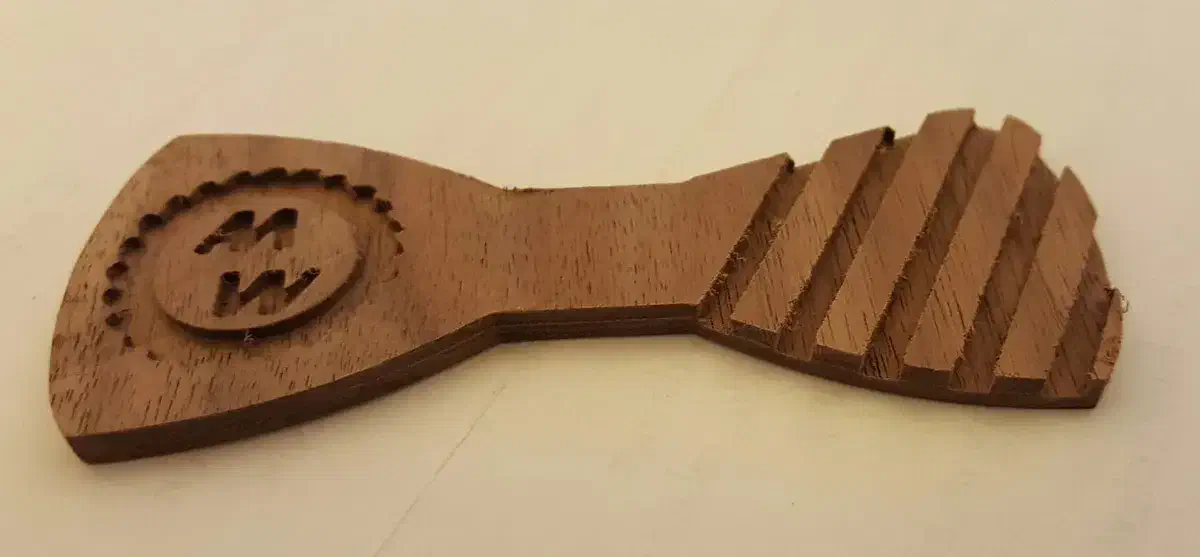 The complete walnut bow-tie cutout has a circular business logo on its left wing and diagonal carved stripes on its right, on a plain cream surface.