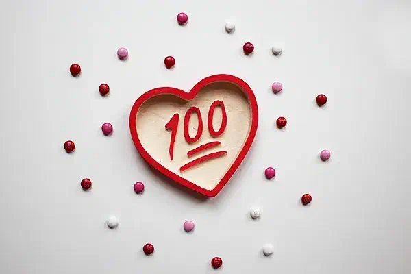 A wooden heart-shaped candy dish with raised red 100 lettering in its recessed center