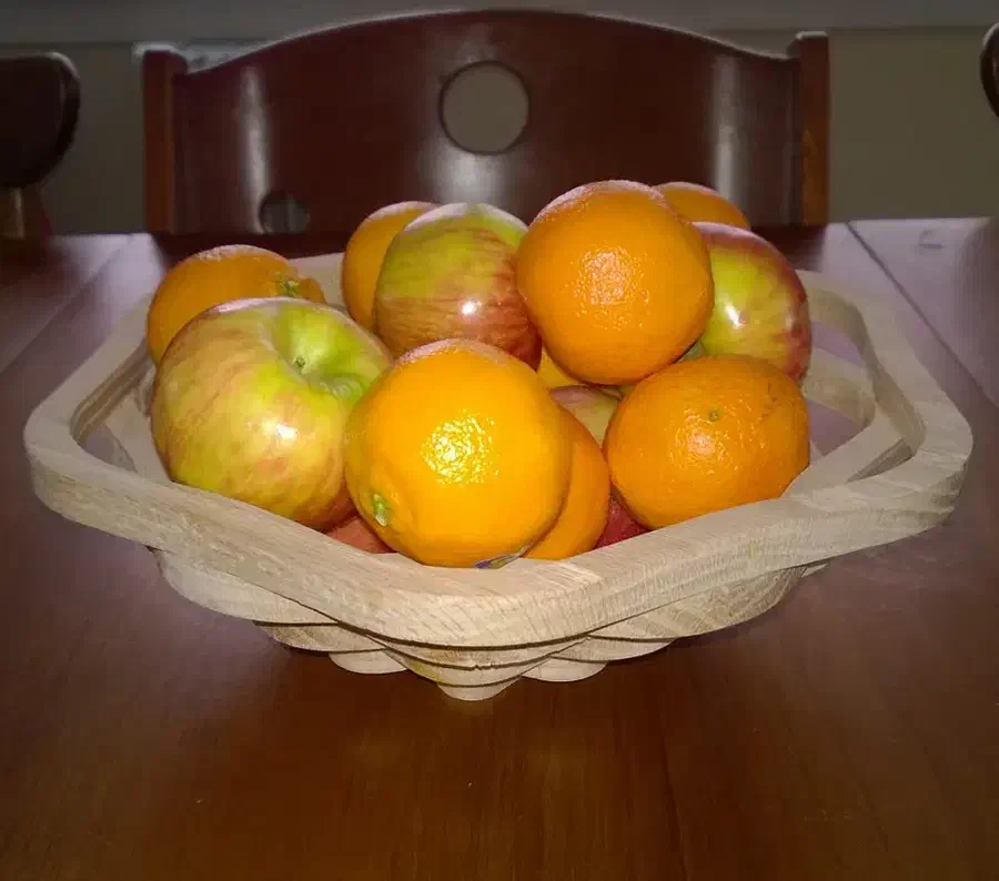 A stacked wooden bowl holding oranges and apples on a dark table
