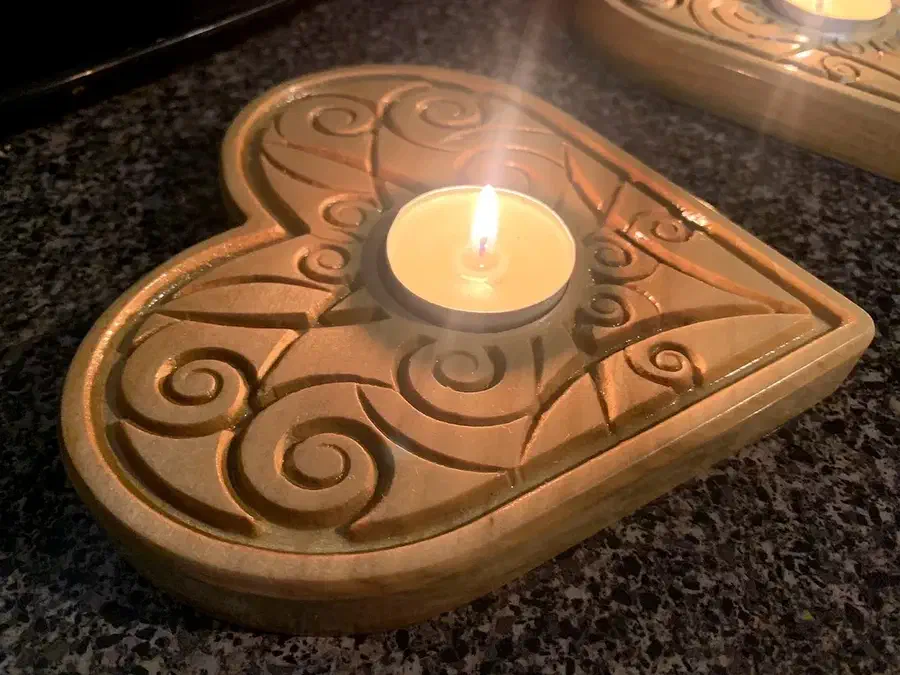 A heart-shaped wooden holder with carved swirls around a single tealight