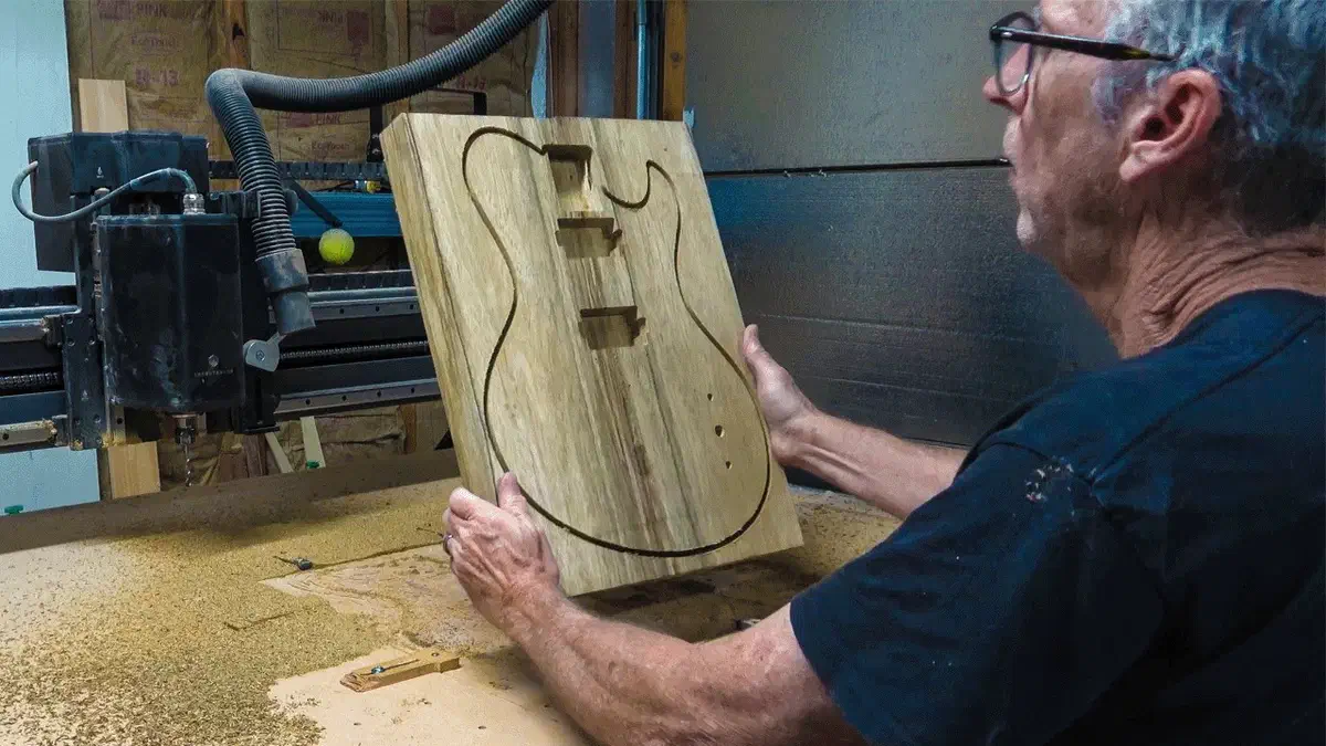 Chris Monck holds a freshly carved guitar body beside his CNC in the Highline Guitars workshop