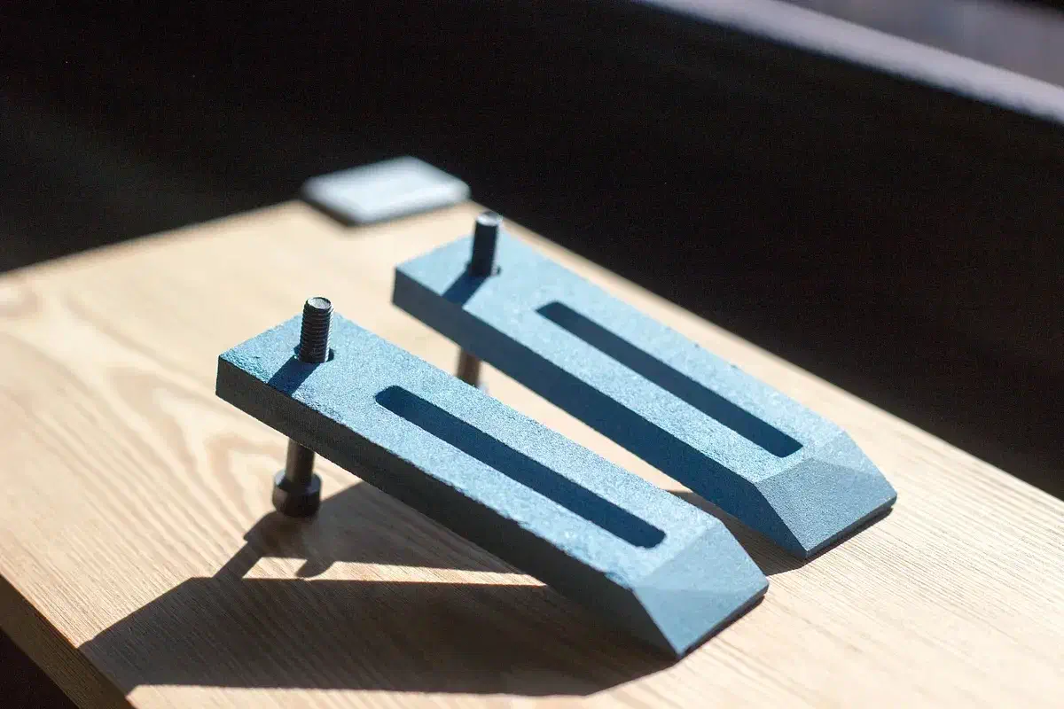 Two blue MDF hold-down clamps with metal screws pressing on a wooden board