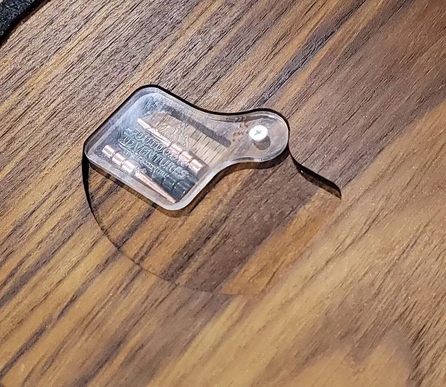 Metal cribbage pegs under a clear pivoting cover recessed into the back of a wooden board