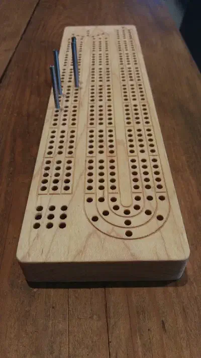 Finished compact hard-maple cribbage board with several peg tracks and two blue pegs