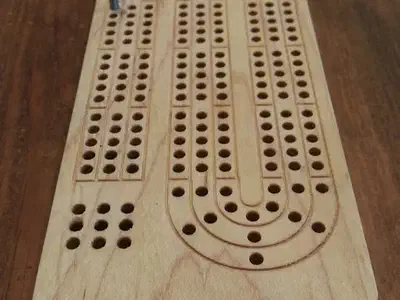 Finished compact hard-maple cribbage board with several peg tracks and two blue pegs