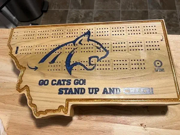 A Montana-shaped wooden cribbage board with a blue bobcat logo and the words Go Cats Go