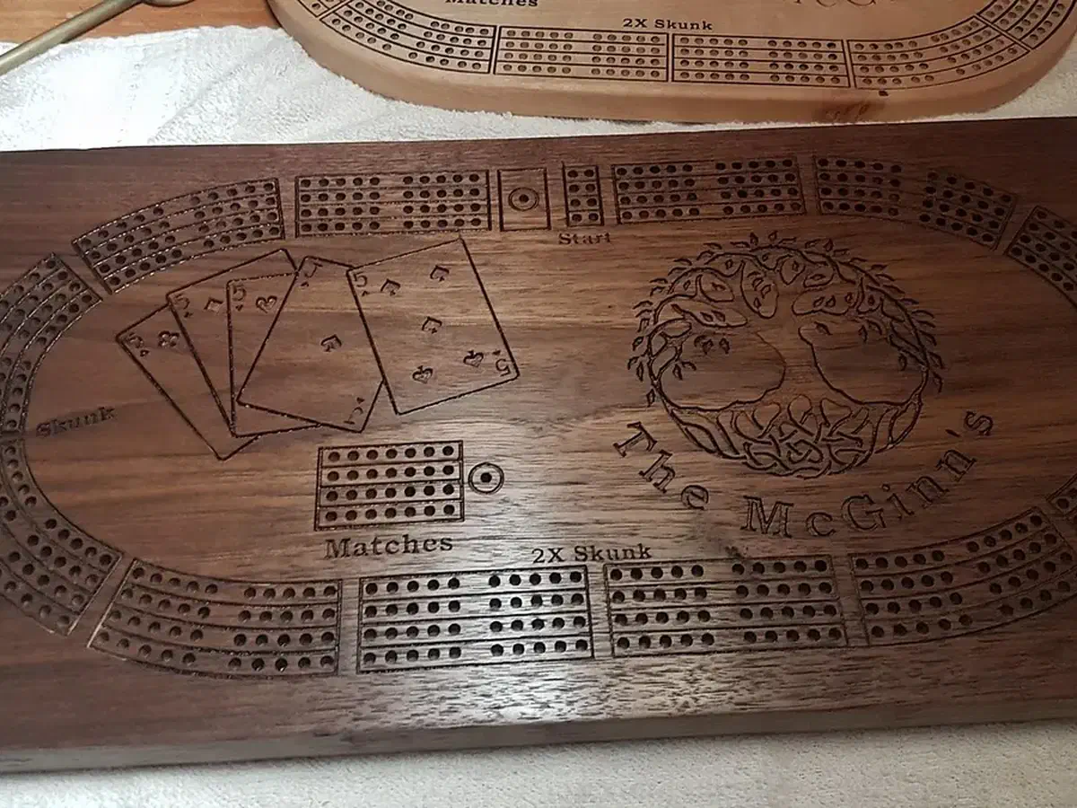 Finished wooden cribbage board with curved peg tracks, playing cards, a carved tree, and the name McGinn