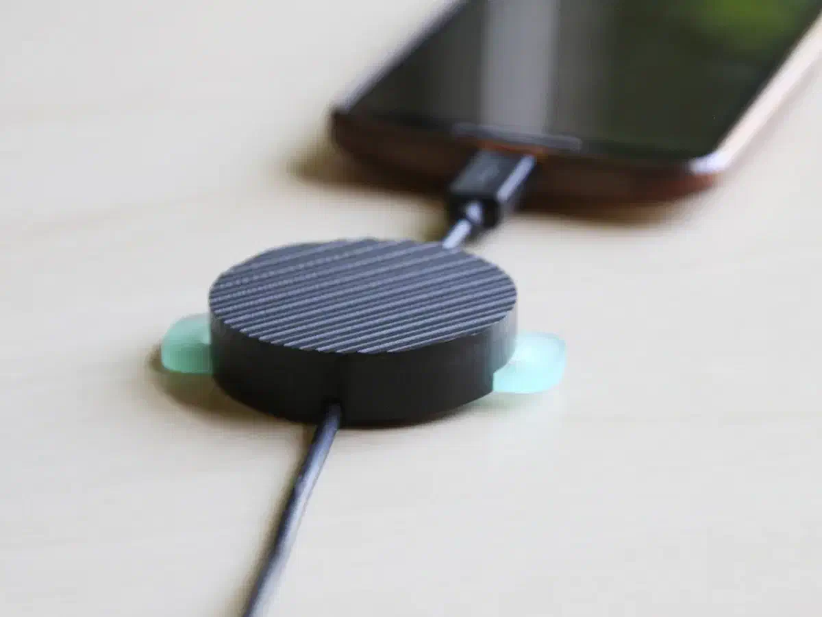 Finished dark cable-management puck holding a charging cable beside a phone