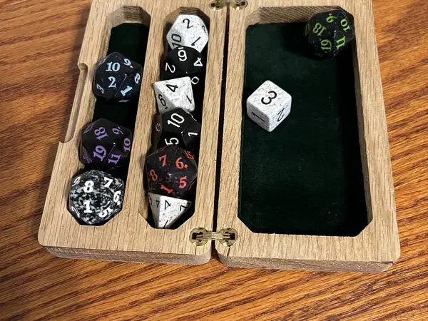 Open hinged wooden dice case with dice stored in two felt-lined rows beside a larger green-felt rolling area