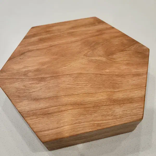 Finished polygonal dice holder carved from light brown wood on a pale surface