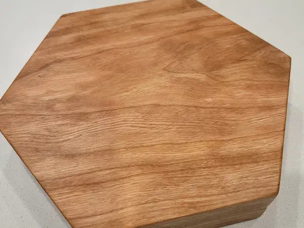 Finished polygonal dice holder carved from light brown wood on a pale surface