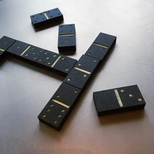 Black domino tiles with gold-colored pips and center lines arranged on a pale tabletop
