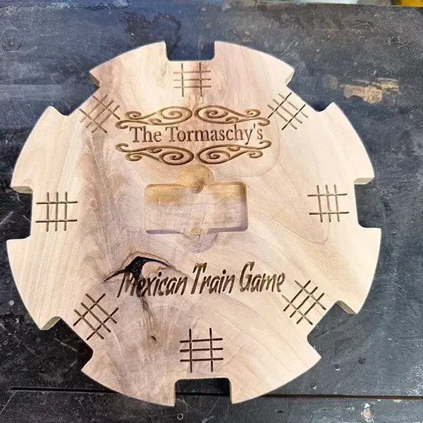 A round wooden Mexican Train hub with eight edge notches, a recessed center and personalized engraved lettering