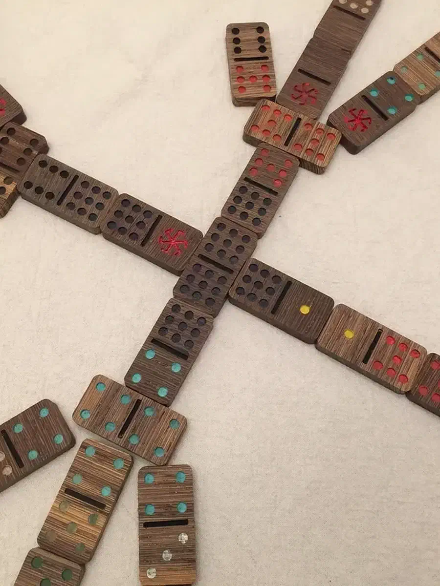 Painted wooden dominoes with colored pips and red spinner symbols arranged in a game on a pale tabletop