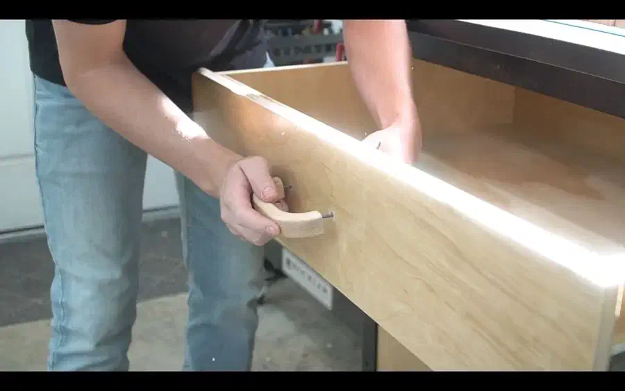 A person opening a plywood drawer by its pale wooden handle