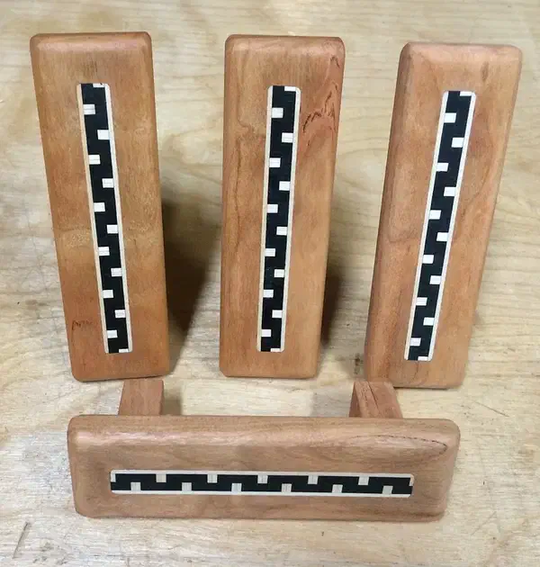 Four finished wooden drawer pulls with black-and-cream patterned inlay strips