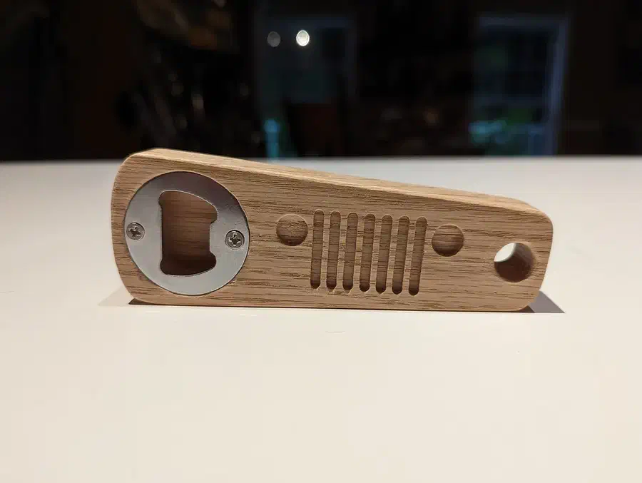 Finished wooden bottle opener shaped like a Jeep grille with a metal insert at one end
