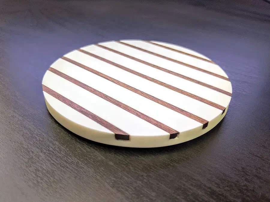 White round Corian coaster with narrow walnut stripes on a dark tabletop