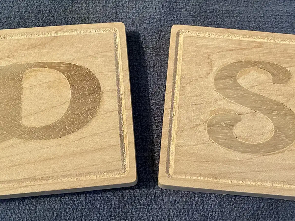 Two square maple coasters with contrasting walnut initial inlays