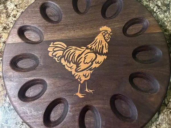 A circular walnut egg holder with twelve recesses and a contrasting cherry chicken inlay