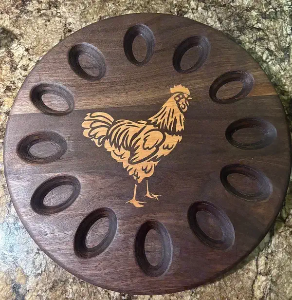 A circular walnut egg holder with twelve recesses and a contrasting cherry chicken inlay