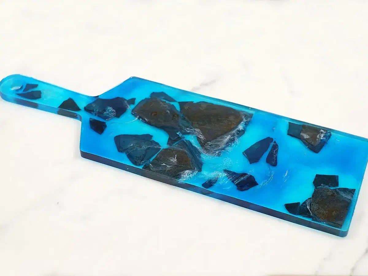 Finished blue resin serving tray with dark embedded pieces and a long handle