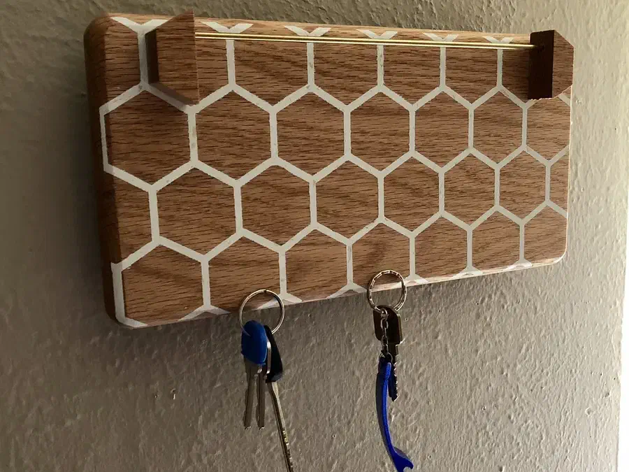 A honeycomb-pattern wooden wall organizer with projecting sunglasses supports, two hanging key rings and a narrow mail slot