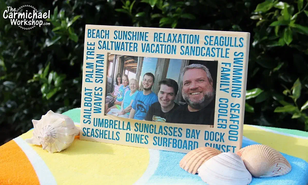 A blue-lettered wooden vacation frame with a curved photograph and clear cover on a table with seashells
