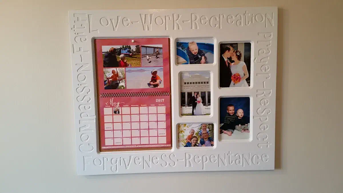 A white wall frame with five family photographs and a calendar surrounded by carved words