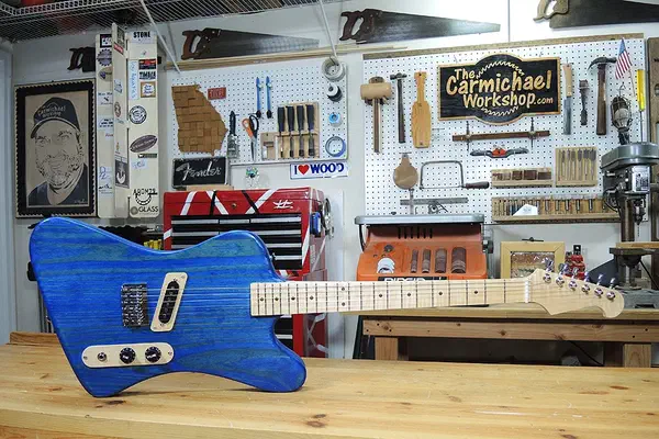 A blue electric guitar with a pale wooden neck resting horizontally on a workshop bench