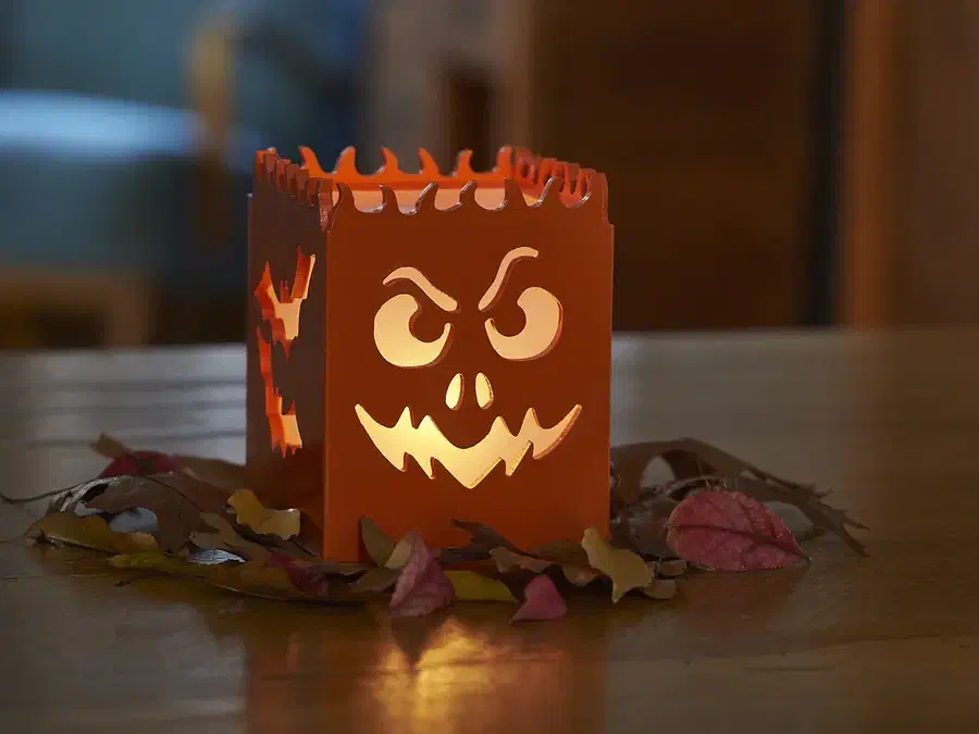Finished orange Halloween lantern glowing through a carved monster face among autumn leaves