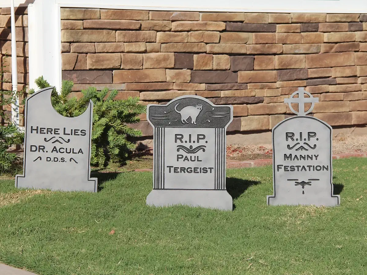 Three finished gray Halloween tombstones with carved names and designs displayed on a lawn